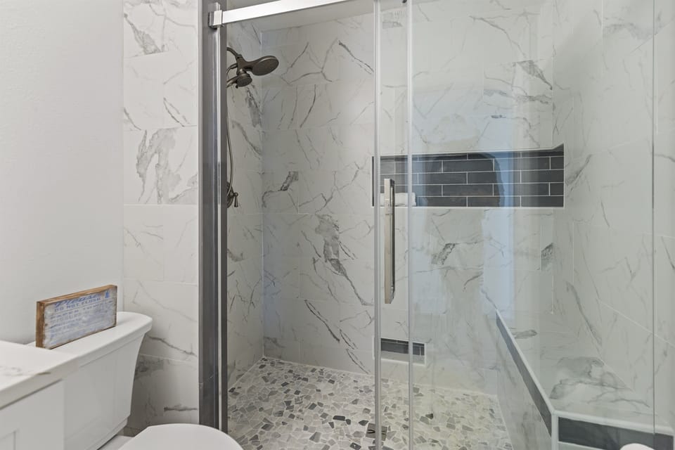 Unwind in your spa-inspired bathroom with marble walls and a spacious glass shower featuring rainfall showerhead and mosaic flooring.