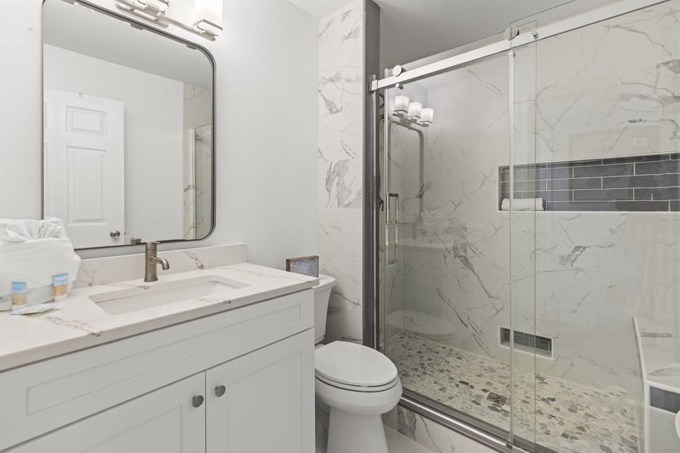 Step into your spa-like bathroom featuring marble walls, a luxurious glass shower, and pristine white vanity for your ultimate comfort.