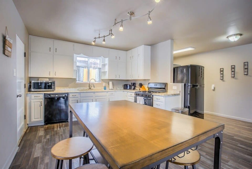 Clean kitchen with white cabinets, stainless fridge, and a long wood island with stools—prep meals with plenty of counter space, serve snacks right on the island, and keep everyone close while you cook and chat.