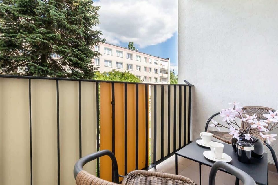 A small balcony with a seating area and a view of the neighborhood, bordered by modern railings.