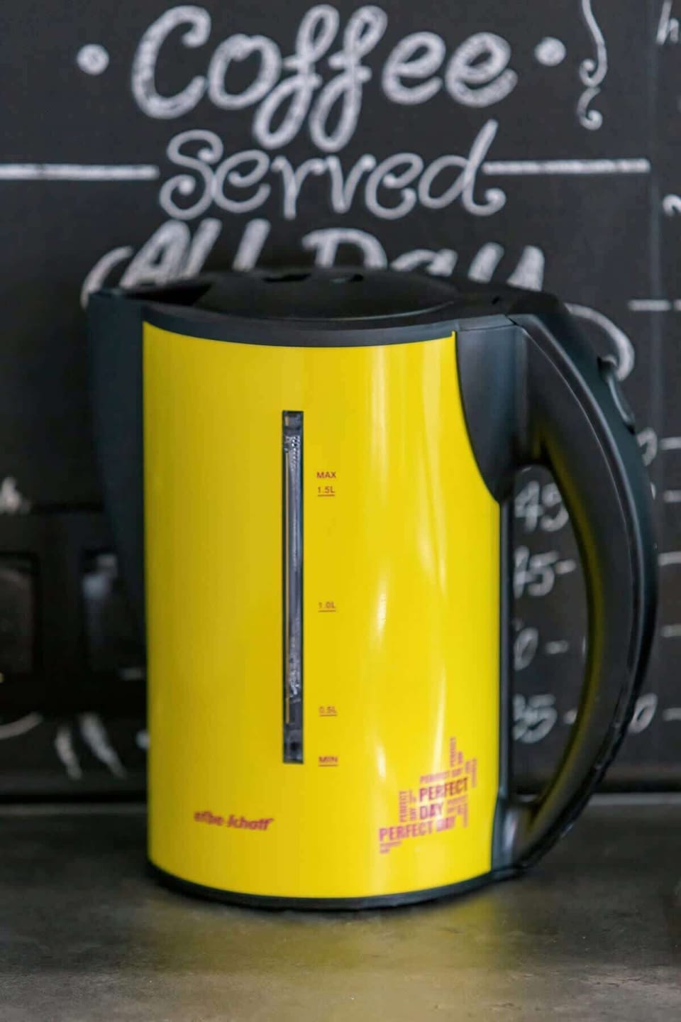 A cheerful kitchen corner featuring a yellow electric kettle and a chalkboard-style decorative wall in the background.