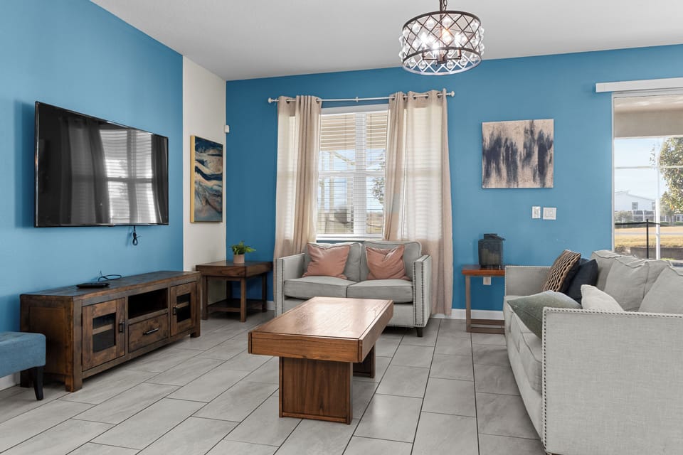 Relax in your bright living room with comfortable seating, modern TV, and beautiful blue accent wall creating a welcoming atmosphere.