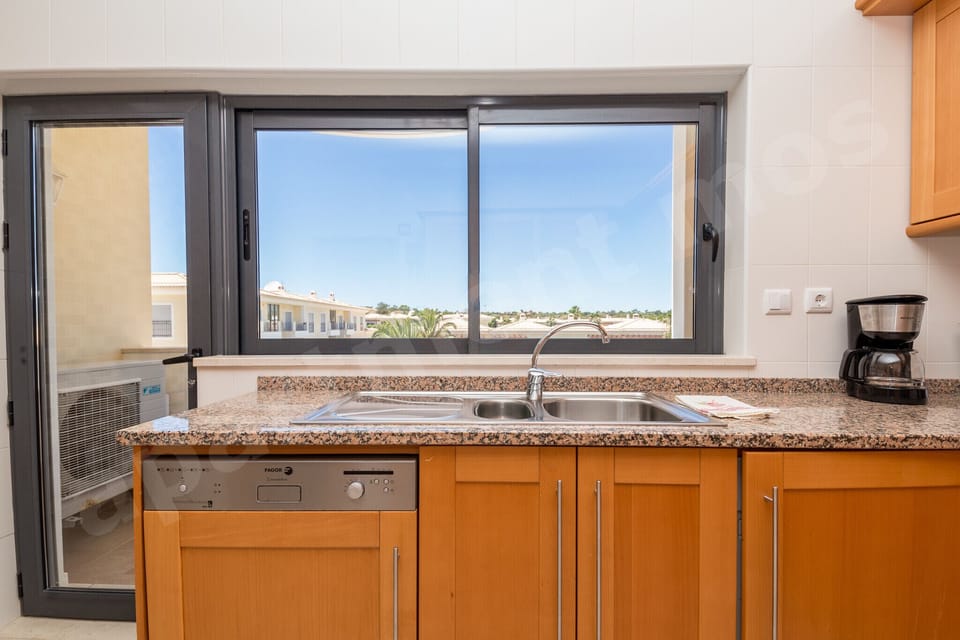 Fully equipped kitchen with wooden cabinets, granite worktops, sink, coffee maker and window views at Apartment Mos, a professionally cleaned 2-bedroom holiday apartment with communal pool in the Algarve, Portugal