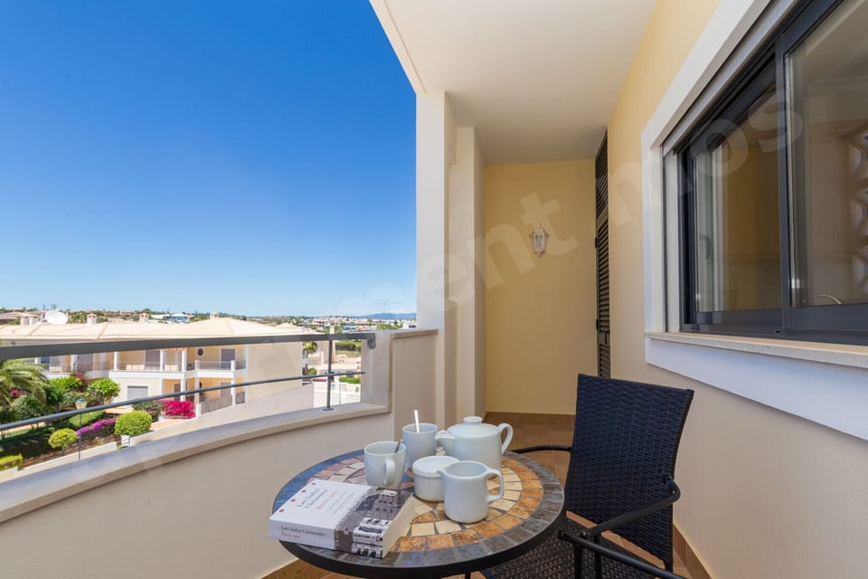 Private balcony with bistro table and tea set at Apartment Mos, offering panoramic views across the Algarve rooftops and lush gardens from this professionally cleaned 2-bedroom holiday apartment in Portugal