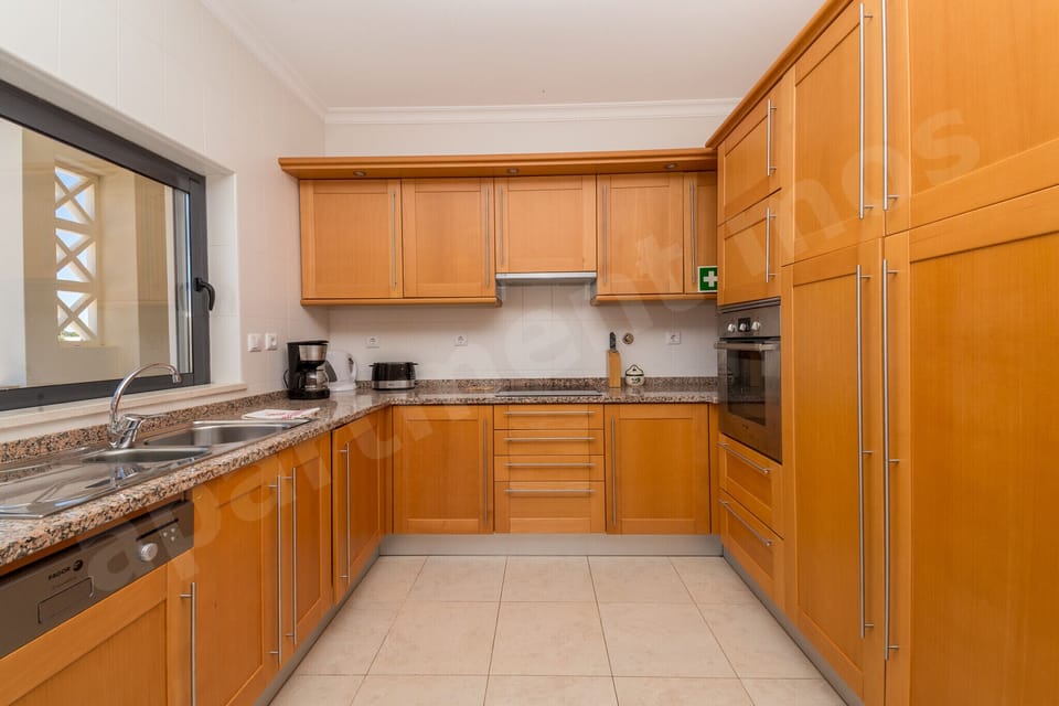 Well-equipped kitchen with stove, oven, wooden cabinetry, granite worktops and tiled backsplash at Apartment Mos, a professionally cleaned 2-bedroom holiday apartment with communal pool in the Algarve, Portugal
