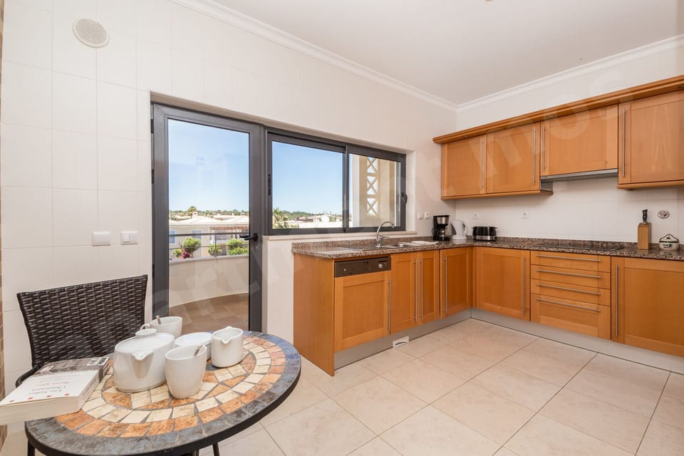 Spacious kitchen with round breakfast table, wooden cabinetry, granite worktops and large window at Apartment Mos, a professionally cleaned 2-bedroom holiday apartment with communal pool in the Algarve, Portugal