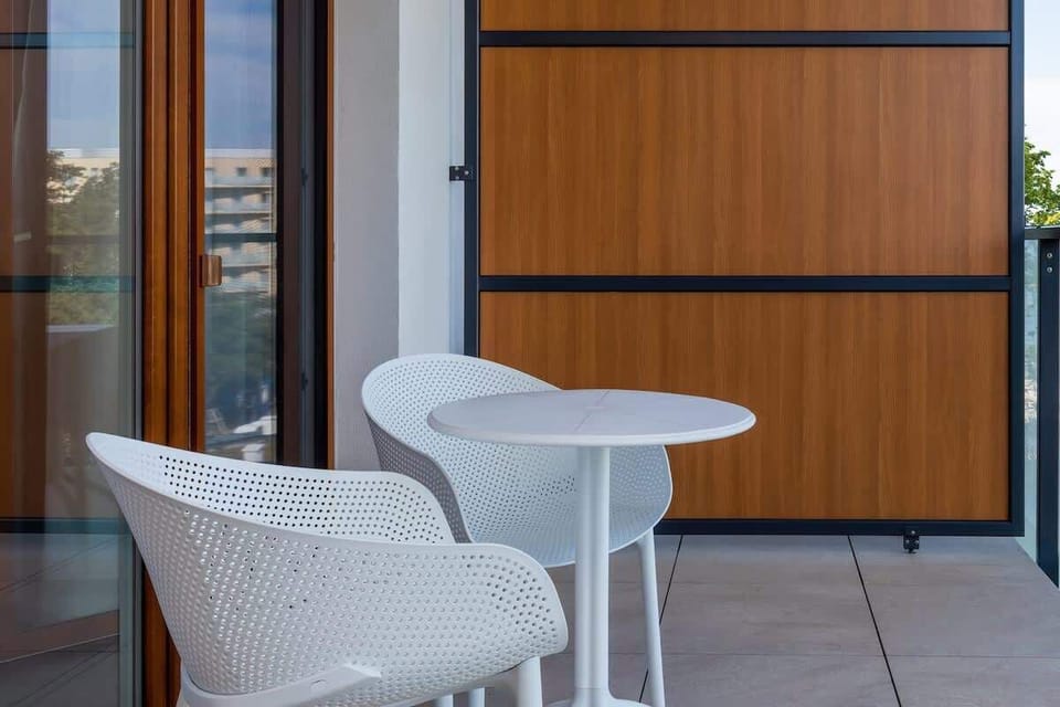 An outdoor balcony with two white chairs and a small table. It overlooks the surroundings, offering a nice place to relax.