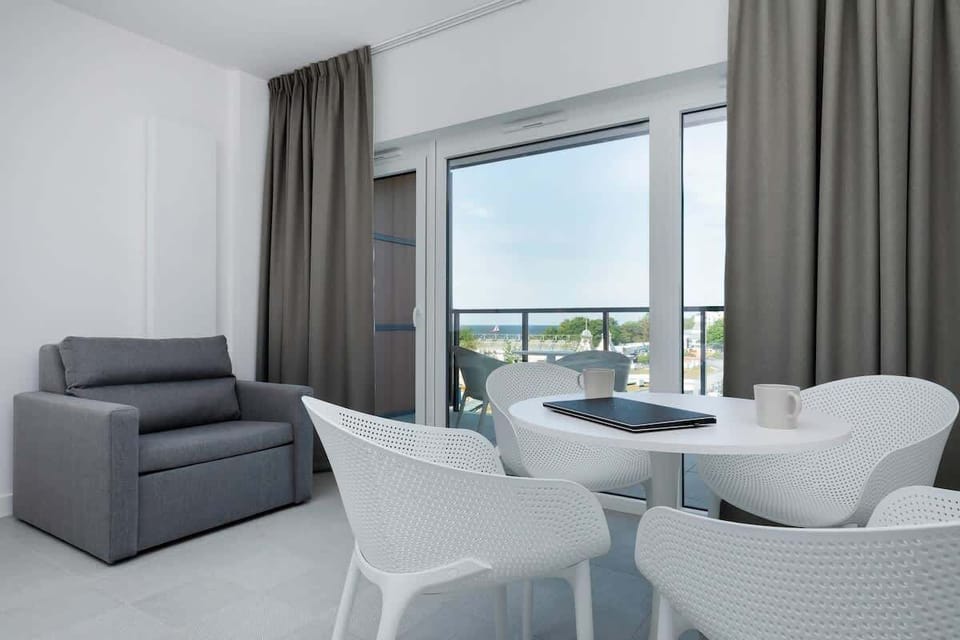 A seating area with armchairs and a coffee table, next to large glass doors that lead to a balcony with an outdoor view.