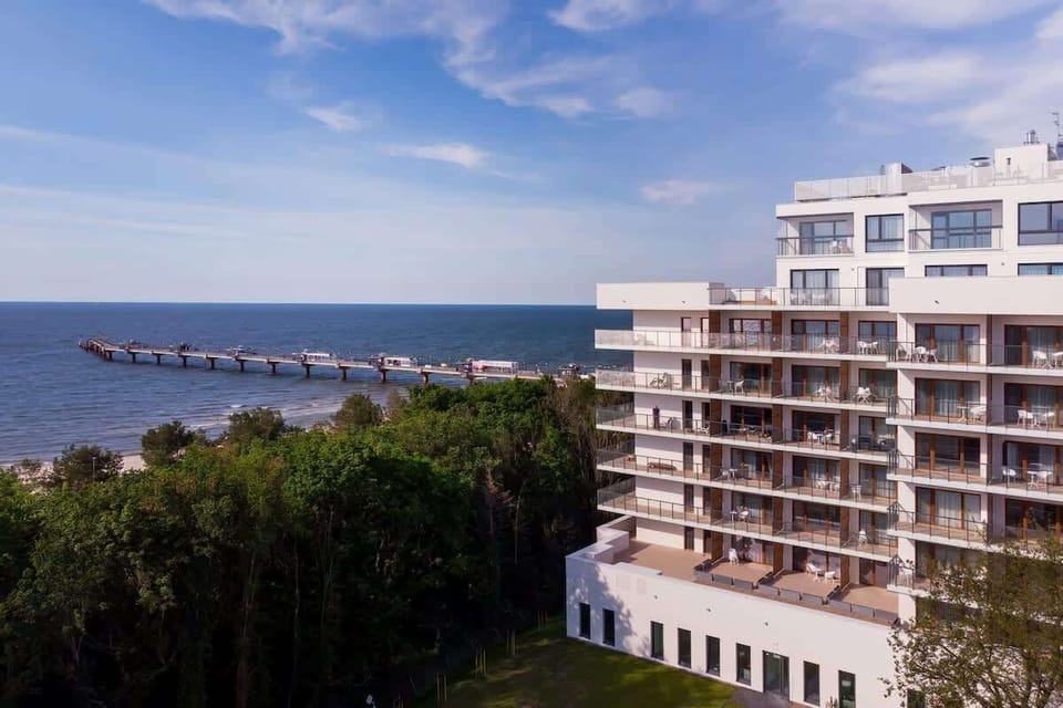 A scenic view of a modern residential building surrounded by greenery, with the sea visible in the background.