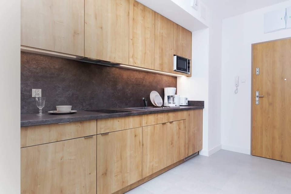 A compact kitchen area with modern wooden cabinets, sleek appliances, and a tiled backsplash. It combines functionality with style.