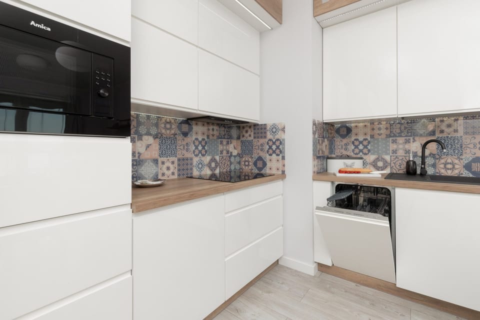 A modern white kitchen with minimalist cabinets and a stylish backsplash. The space is bright and organized, giving a clean and fresh impression.