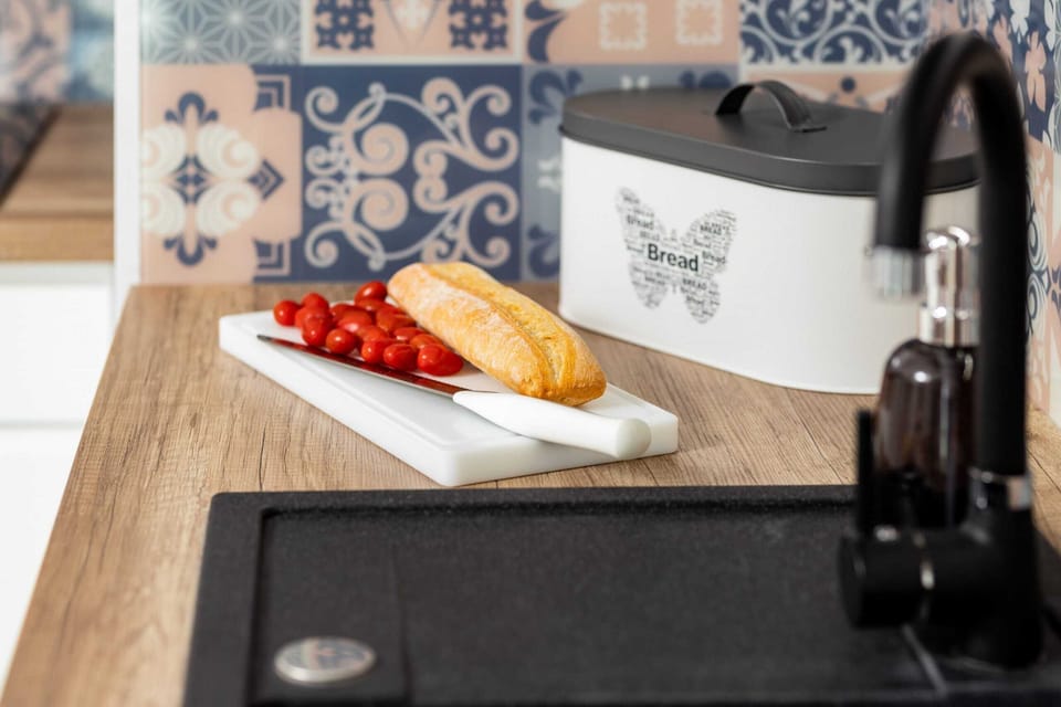 A close-up of a kitchen countertop with a sink, a cutting board, and fresh fruit. The backsplash has blue and white patterned tiles, adding character to the kitchen.
