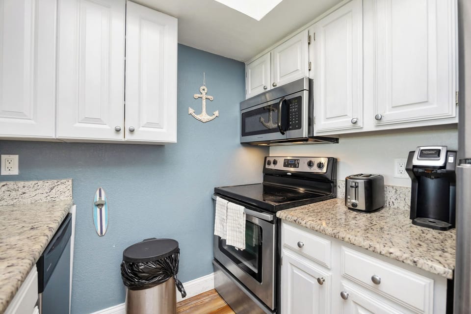 Your coastal kitchen awaits with nautical charm - white cabinets, granite counters, and full appliances for preparing seaside feasts.
