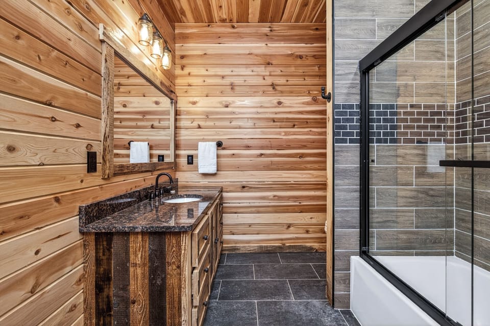 Your rustic bathroom retreat features warm cedar walls, granite countertops, and a luxurious glass-enclosed tub where you can unwind.