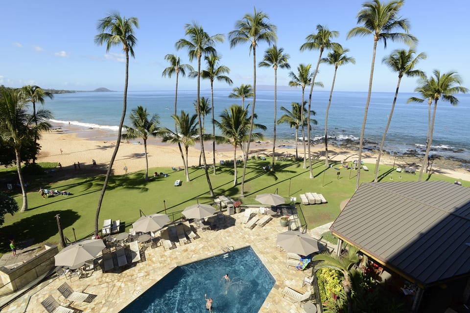 Bird's eye view of the pool with tables and umbrellas, lawn, beach and the ocean