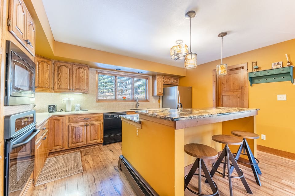 Your fully equipped kitchen features warm wood cabinets, granite countertops, and a breakfast bar perfect for morning coffee or casual meals together.
