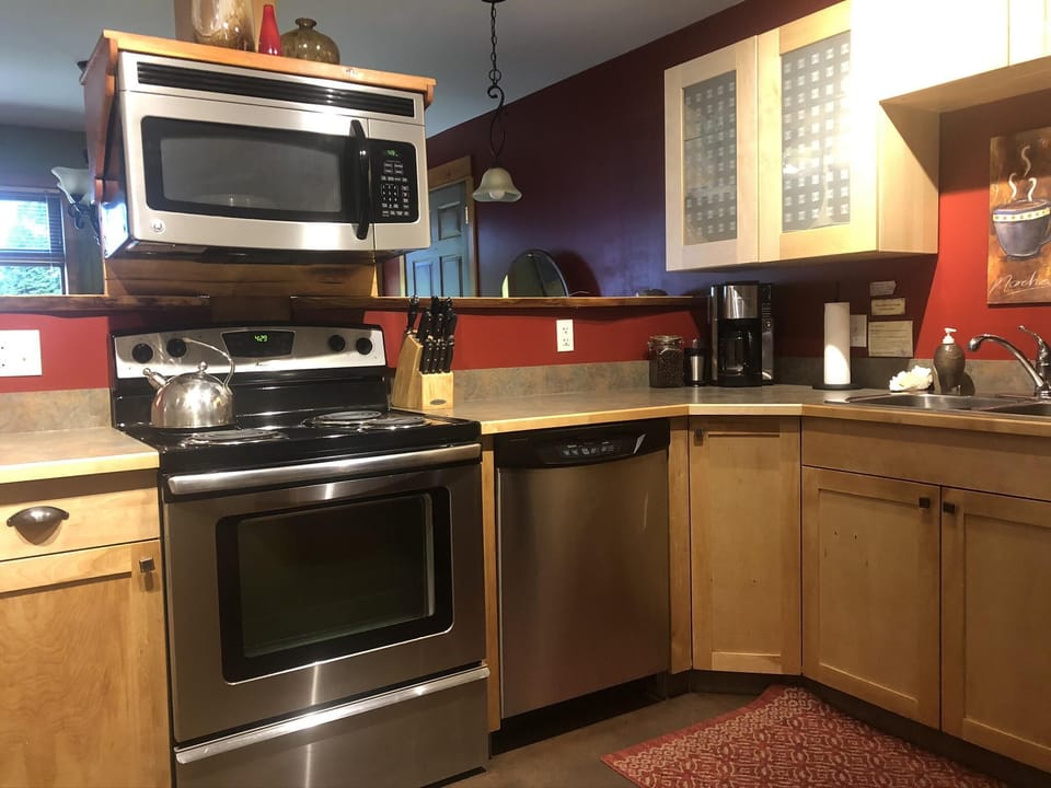 Stainless steel appliances, maple cabinetry, and red accent walls frame the kitchen’s corner layout.