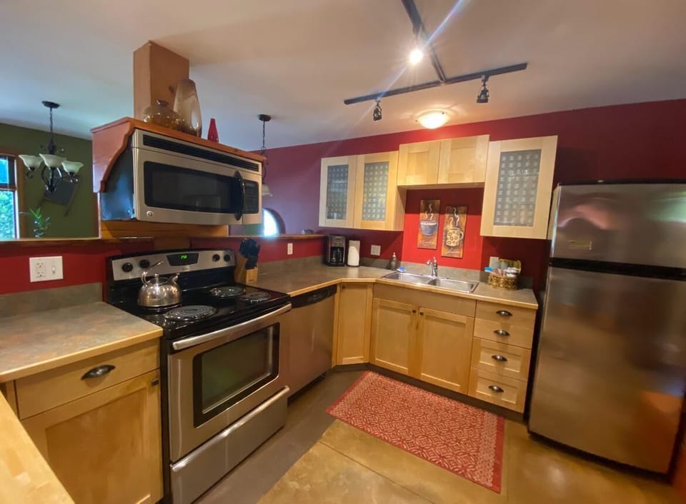 Track lighting and a flush ceiling fixture illuminate maple cabinets with frosted glass fronts and a double sink.