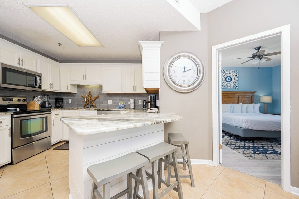 Bright kitchen features a marbled countertop, sleek appliances, and a breakfast bar with seating, leading to the master suite