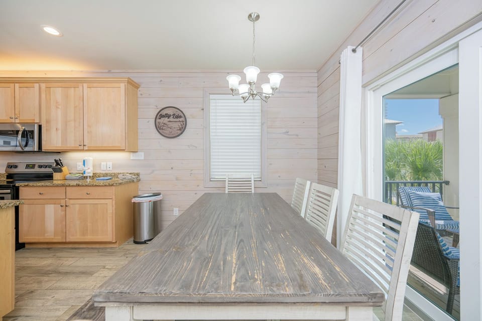 Bright dining area featuring a rustic table, modern kitchen amenities, and a view of lush greenery through sliding doors