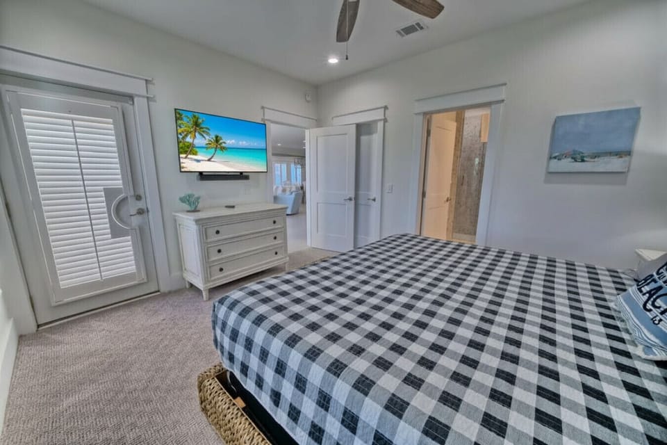 Master bedroom with king bed, wall-mounted TV, dresser, private balcony access, en-suite bathroom. Panama City Beach vacation rental.