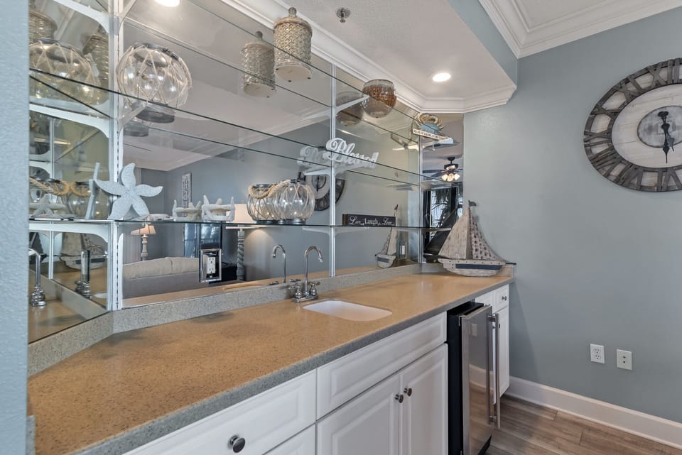 Perfect for entertaining, this stylish wet bar features a mini-fridge and a sink for convenience. With beautiful coastal decor and a reflective mirror backdrop, it's a dedicated space to mix drinks and toast to a perfect getaway.