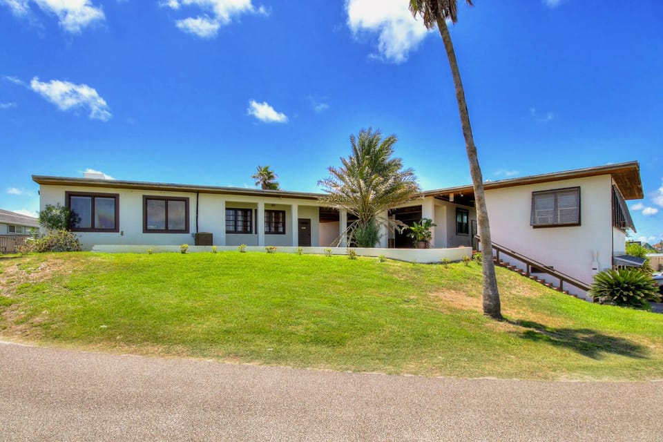 Single-story tropical vacation home with spacious grounds, palm trees, and modern comfort under brilliant blue skies.
