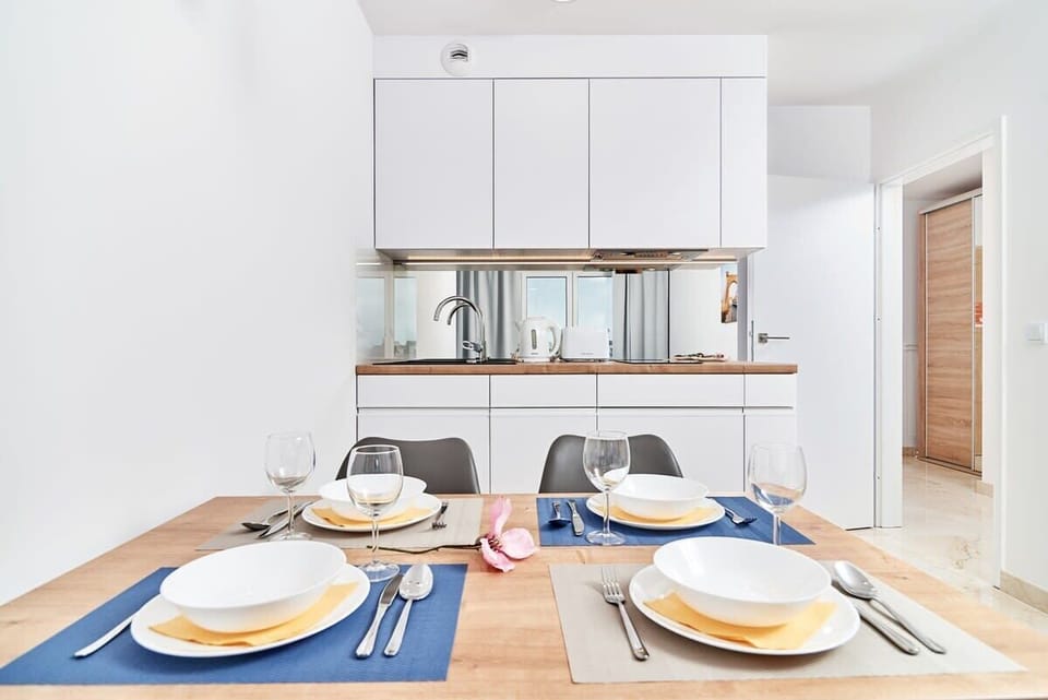 A stylish dining area with a wooden table and gray upholstered chairs, next to a fully equipped kitchen.