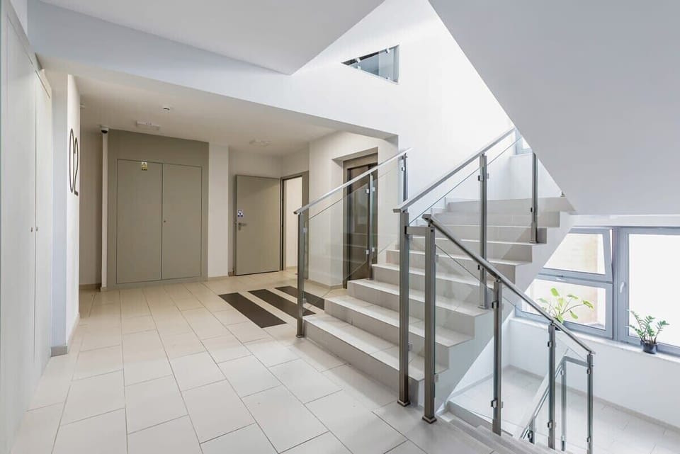 An interior shot of an apartment building, showing stairs, a rail, and tiled floors.