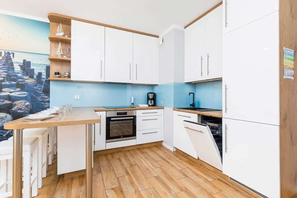 A compact kitchenette with white cabinetry, a blue backsplash, and modern appliances like an oven and fridge.