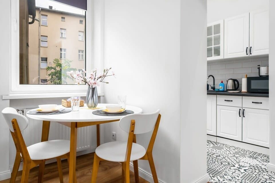 A dining table set for two near a window, surrounded by light wood chairs, creating a bright and inviting space.