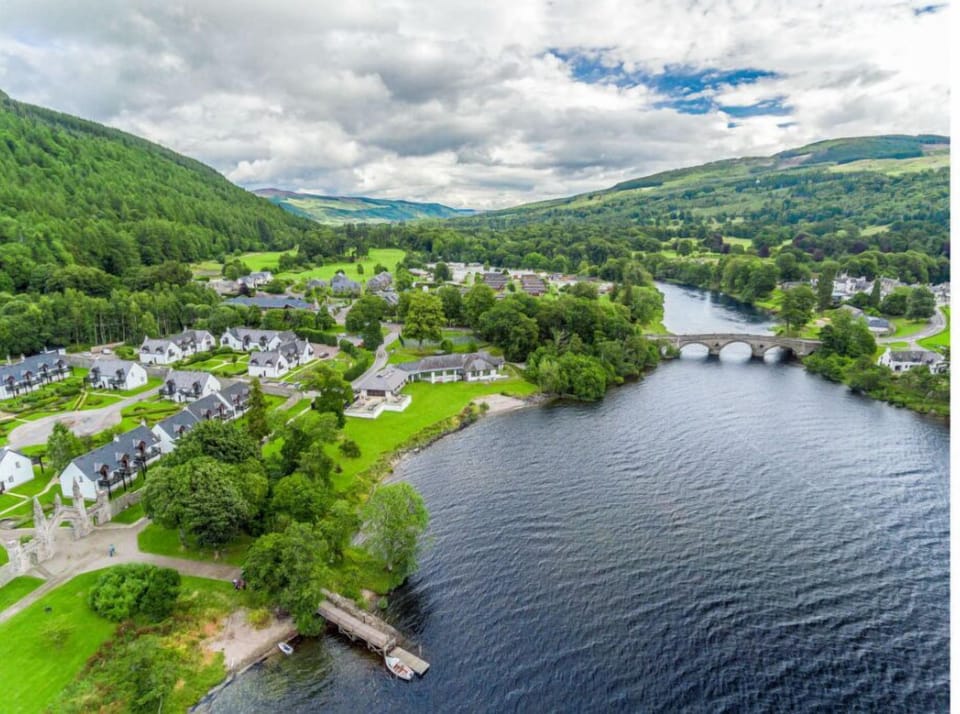 Aerial view of a scenic riverside community with lush landscapes and a charming stone bridge.