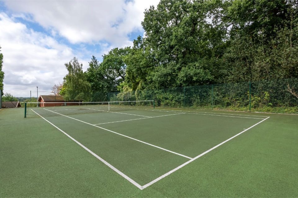 A well-maintained tennis court set within a green landscape, ideal for sports enthusiasts.