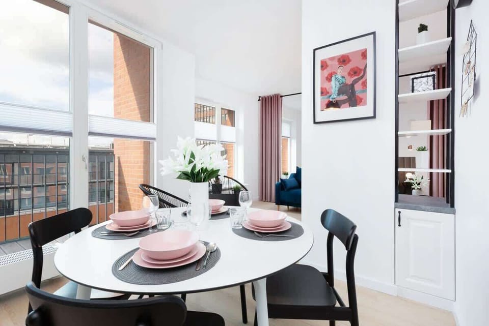 A dining table set with pastel pink plates and modern cutlery, complemented by floral decorations.