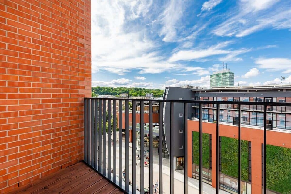 A balcony showcasing a view of surrounding architecture, highlighted by a red brick wall and a modern railing.