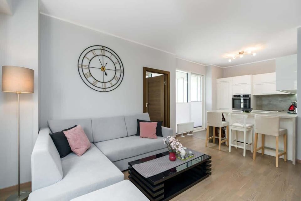 A well-lit living room showcasing the gray sectional sofa, decorative pillows, and a wall clock.