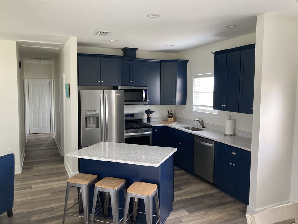 Kitchen area with island with 3 chairs plus stainless steel appliances.