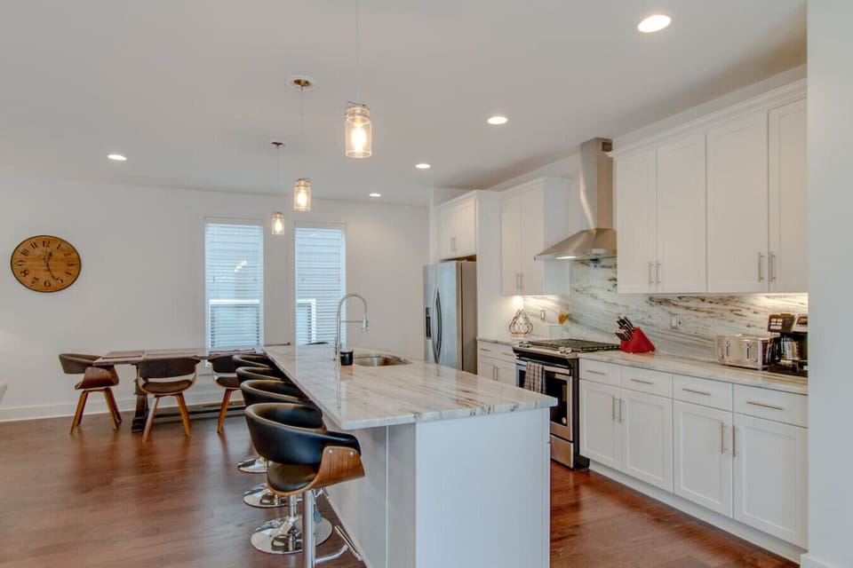Kitchen with white cabinetry, marble island, bar stools, and stainless steel appliances