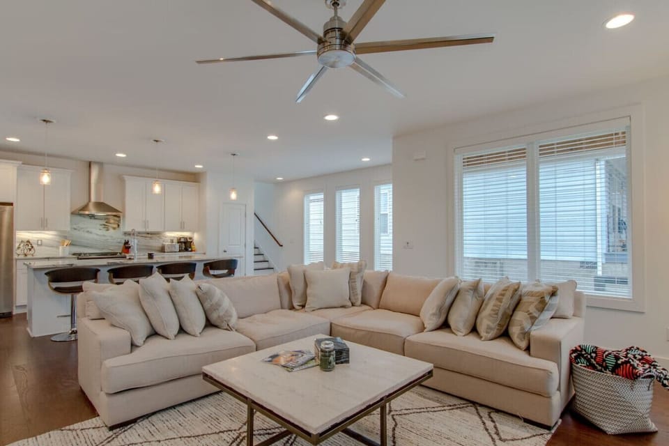 Spacious living room with large cream sectional, ceiling fan, and open kitchen