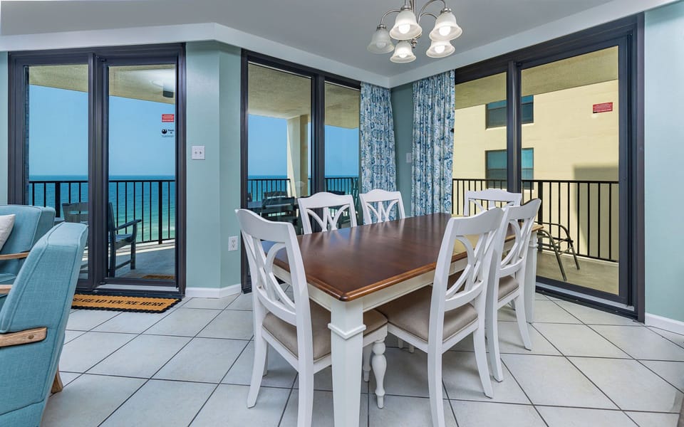 A stylish dining table with six chairs and large windows showcasing a beach front view