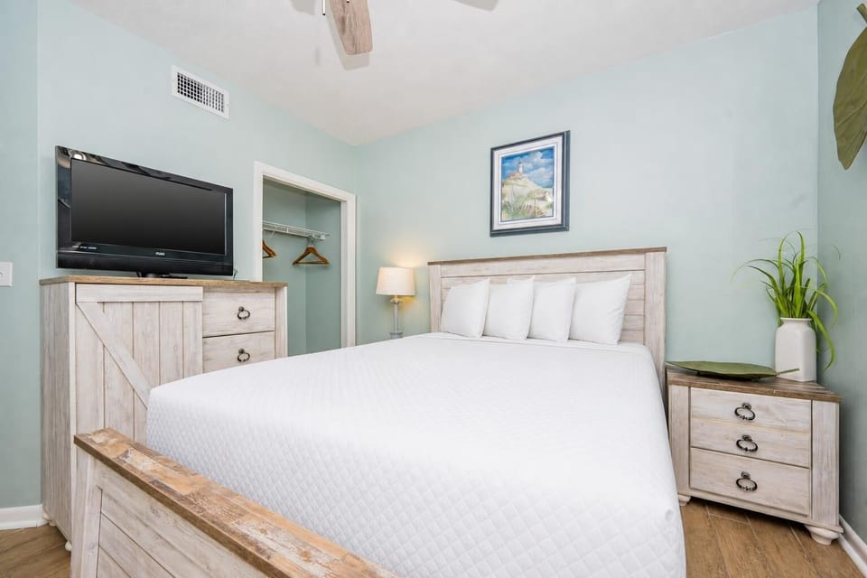 Rest in this serene guest bedroom featuring a comfortable queen bed, a TV, and coastal art for a relaxing getaway