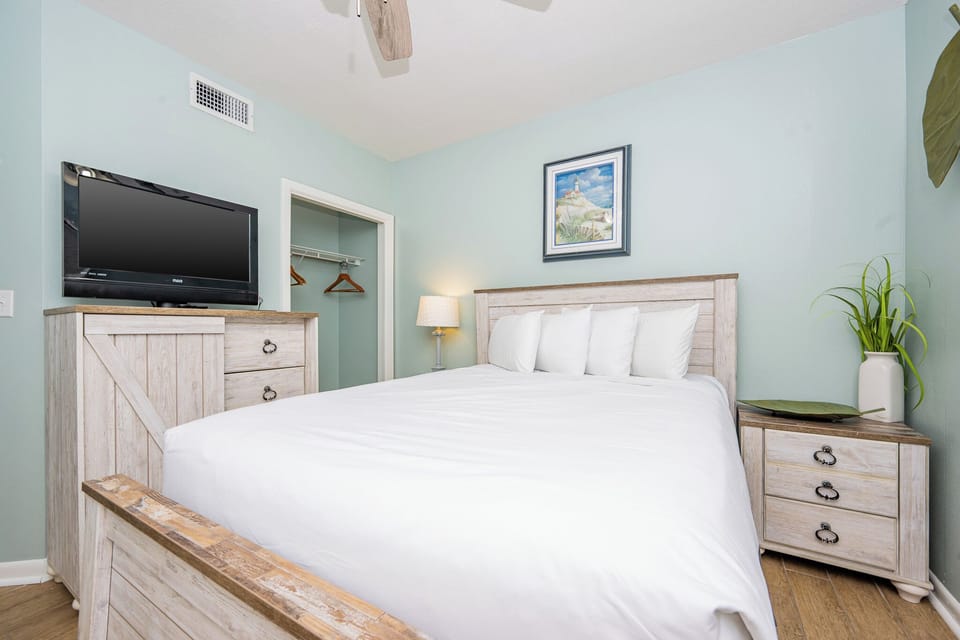 Rest in this serene guest bedroom featuring a comfortable queen bed, a TV, and coastal art for a relaxing getaway