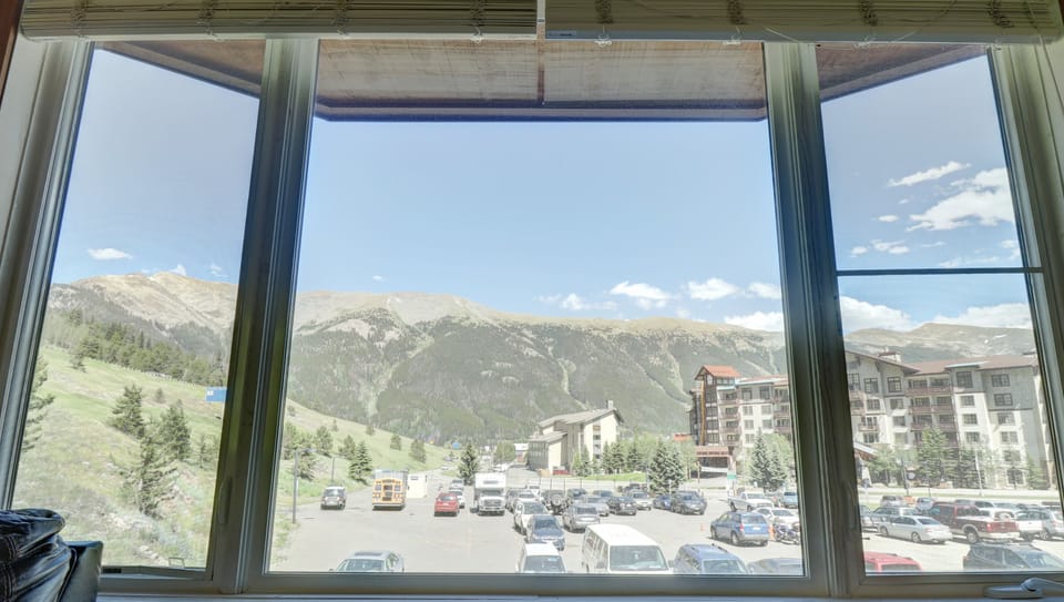 View through a large window showing a parking lot, buildings, and a mountainous landscape under a clear blue sky.