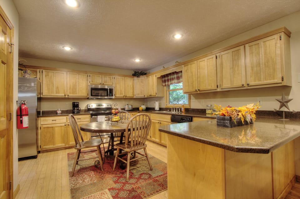 Spacious cabin kitchen with granite counters, stainless steel appliances, coffee maker, full cookware, and dining space. Perfect for family vacations in Pigeon Forge, Gatlinburg & the Smoky Mountains!