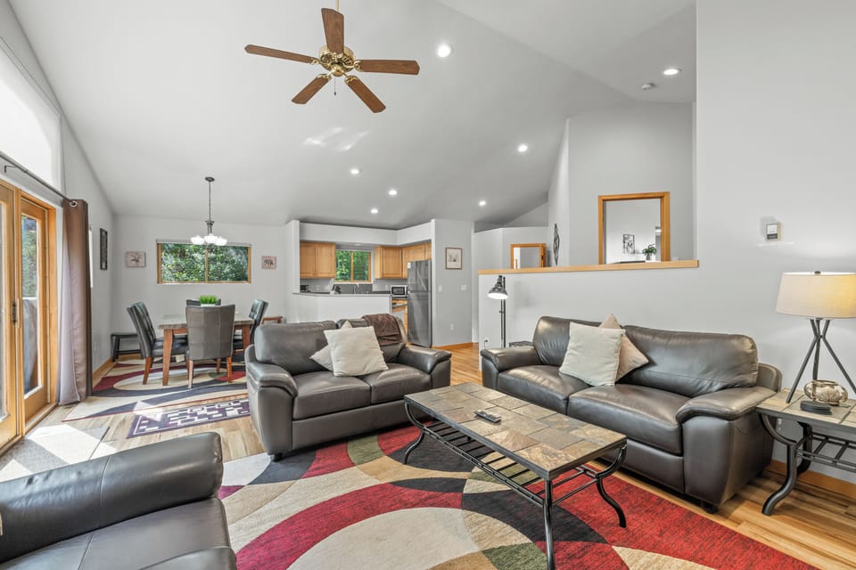 Bright open-concept living space featuring plush leather seating, vaulted ceilings with ceiling fan, and a seamless flow into the dining and kitchen areas for effortless entertaining.