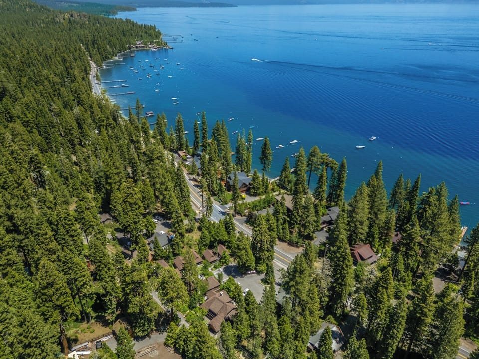 Aerial view of the lakeside neighborhood with vacation rentals nestled among towering pines along crystal-clear waters, featuring boat access and stunning natural surroundings.