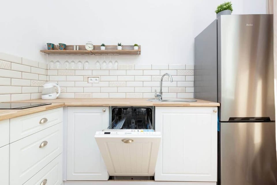 A kitchen corner with white cabinets, a refrigerator, and a tiled backsplash. The setup is compact and modern.
