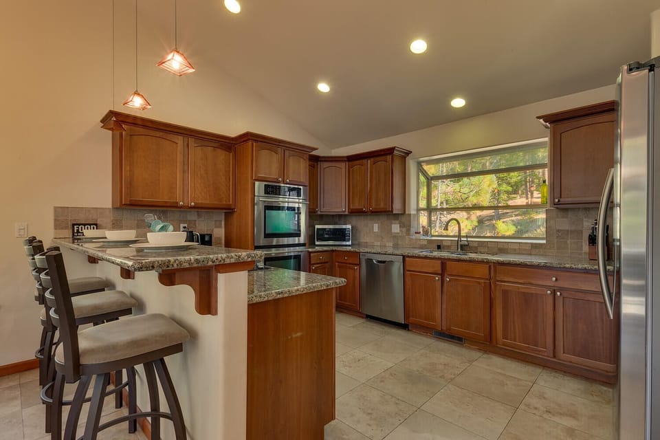 - Kitchen with granite counters and modern appliances  
- Stainless steel oven, dishwasher and fridge setup  
- Spacious bar seating with warm wood cabinetry