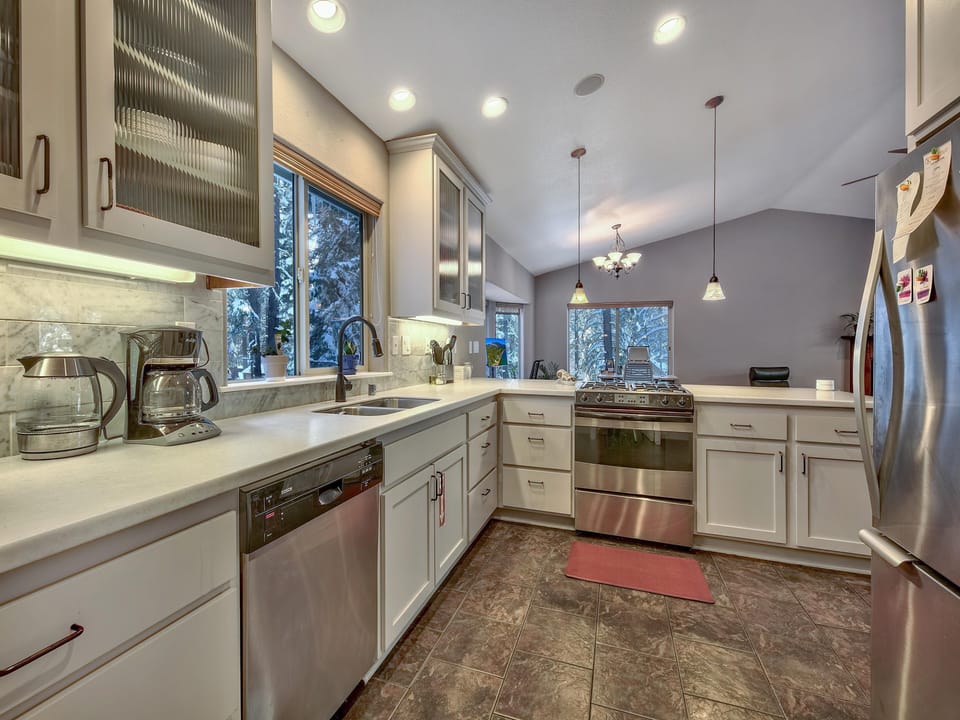 Galley kitchen with white cabinetry, stainless steel appliances, marble backsplash, and large windows showing snowy trees.