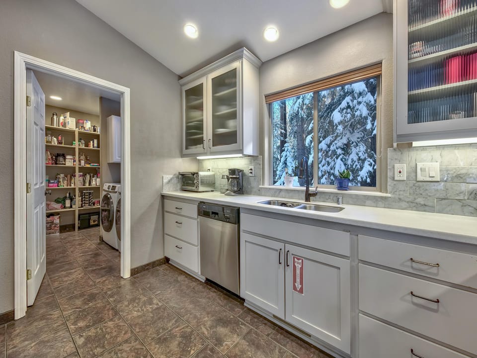 Tile floor kitchen with under-cabinet lighting, stainless steel dishwasher, and a double sink under a snowy window view.